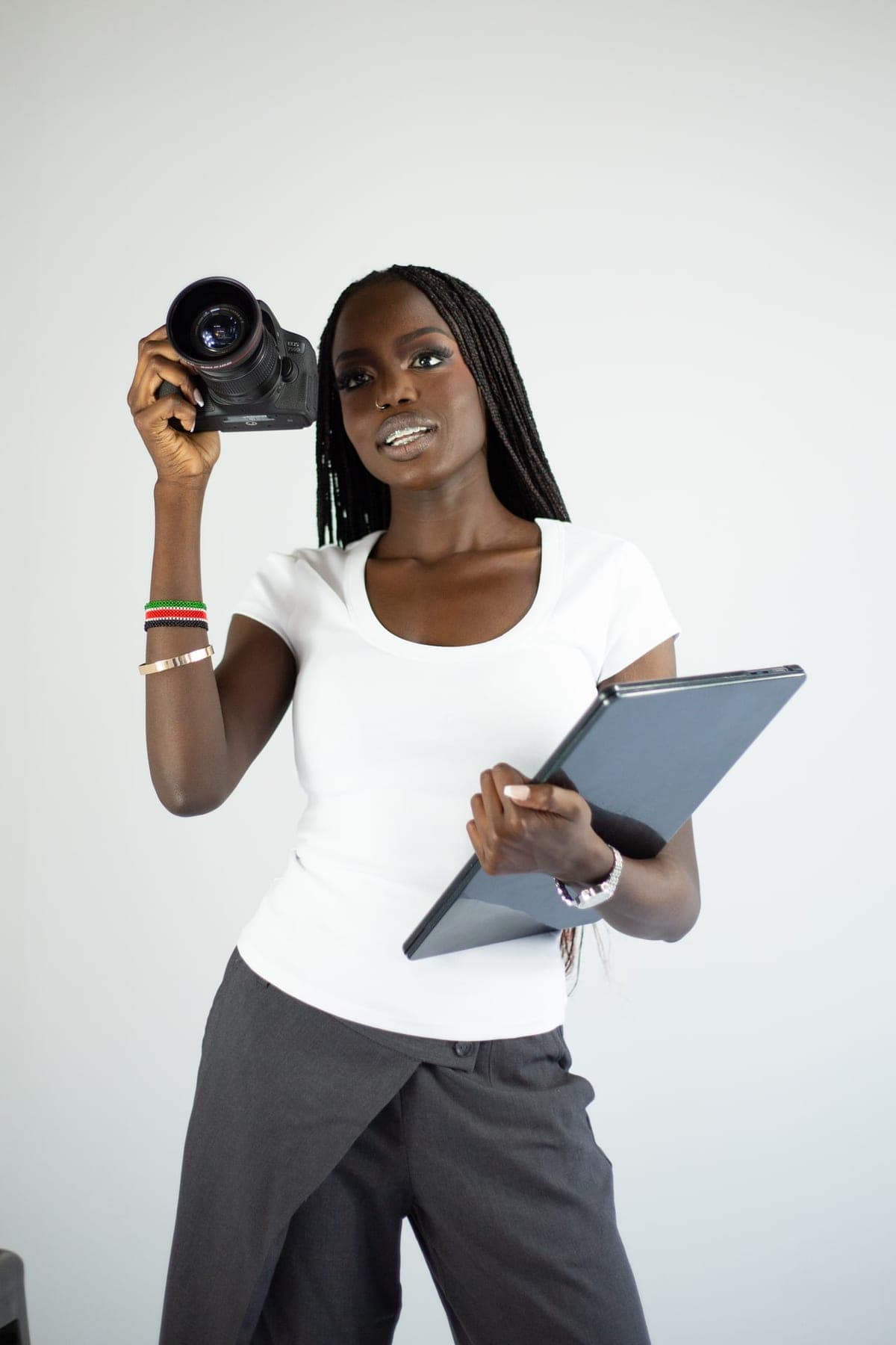 Akoi Chol in the studio, holding a camera up beside her face and a tablet in her other hand.