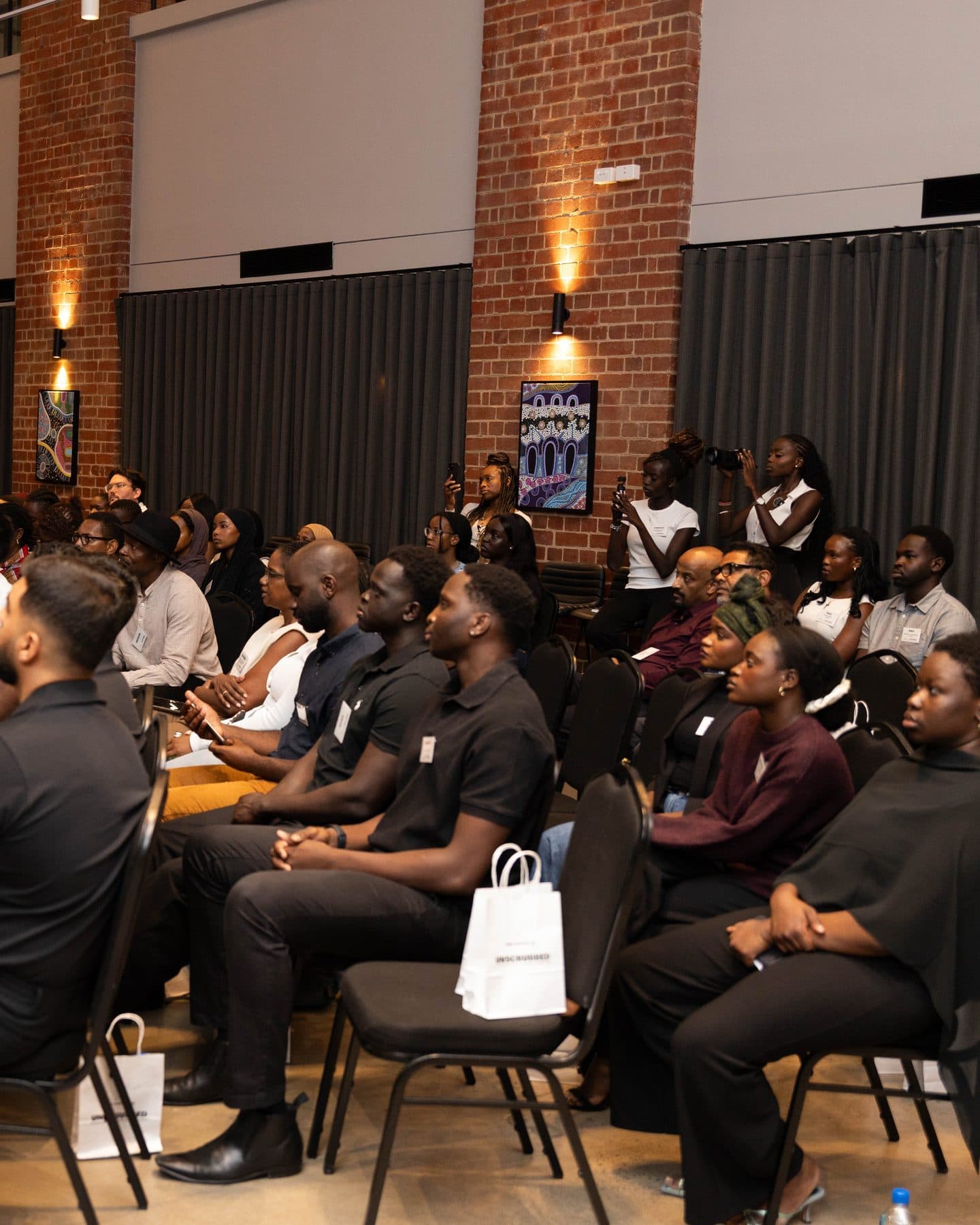 A full room of guests seated in rows at UNSCRUBBED, under brick walls and warm wall lights.